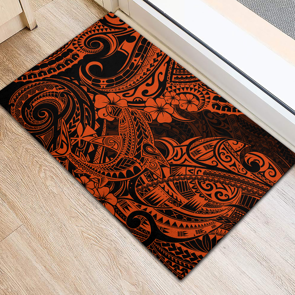 Orange and black polynesian patterned rubber doormat laid flat on light wood floor.