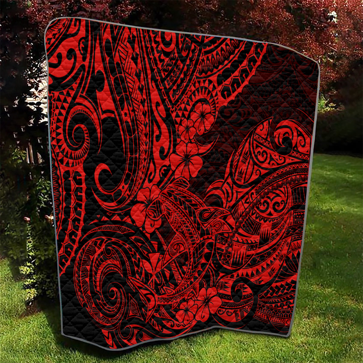 Red and black Polynesian shark pattern quilt, square blanket draped on grass.