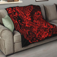 Red and black Polynesian shark pattern quilt, folded on beige sofa arm.