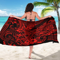 Red and black tribal-pattern sarong wrap with swirling designs, worn on beach