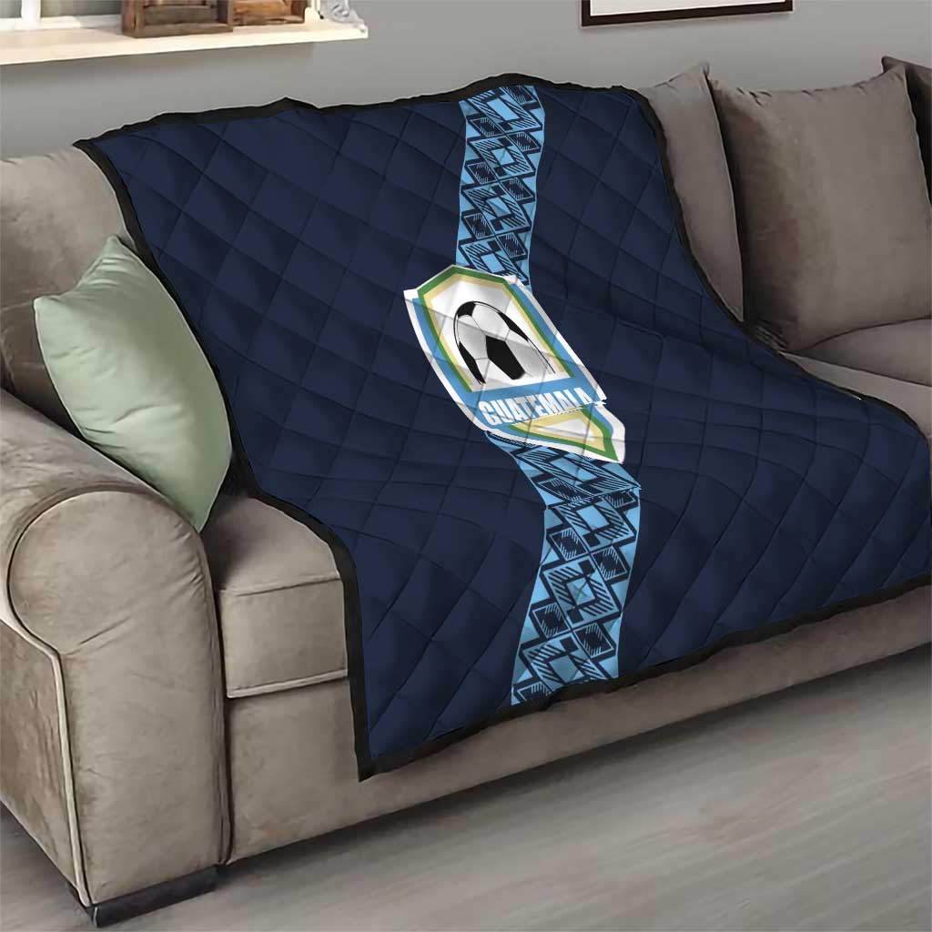 Navy football quilt draped on sofa, diamond quilting with diagonal blue stripe and Guatemala crest