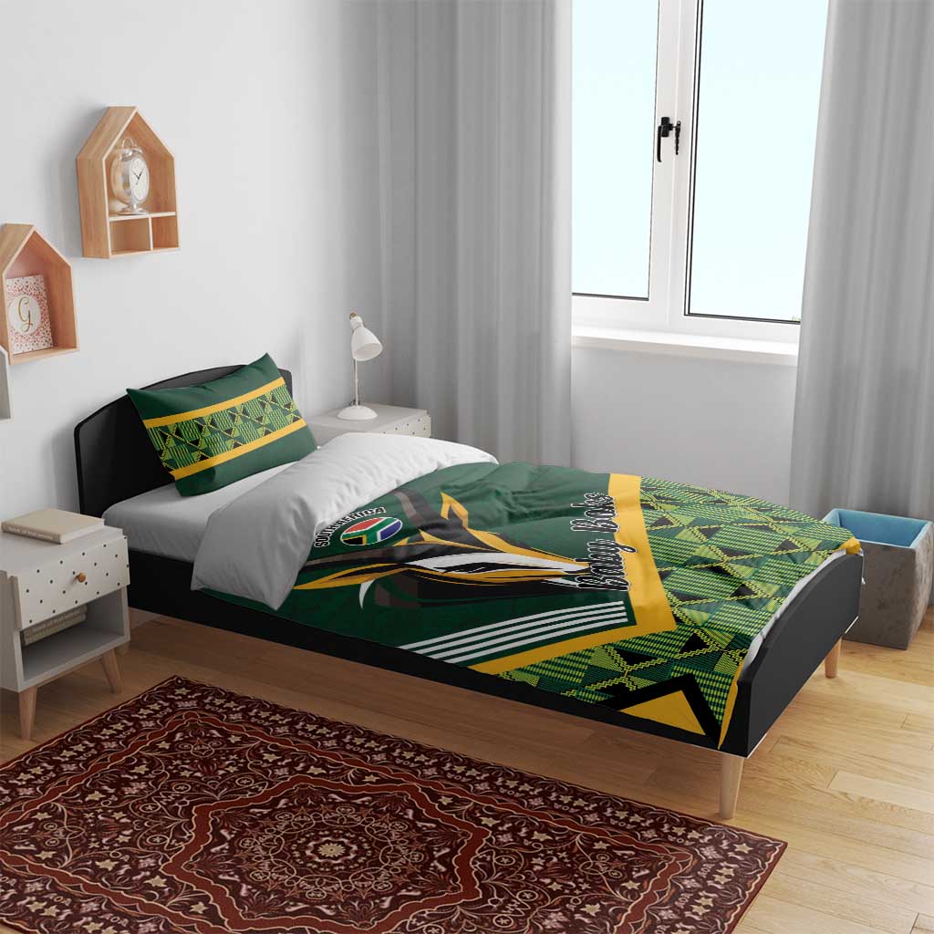 Green baby bedding set on bed with rugby logo, yellow accents, and geometric plaid design