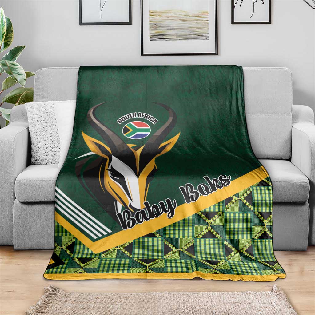 Green baby blanket draped on gray sofa, 'Baby Boks' emblem and plaid