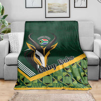 Green baby blanket draped on gray sofa, 'Baby Boks' emblem and plaid
