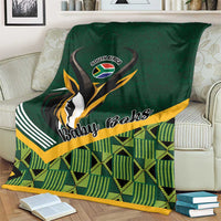Green baby blanket on cream sofa with 'Baby Boks' emblem and tartan pattern