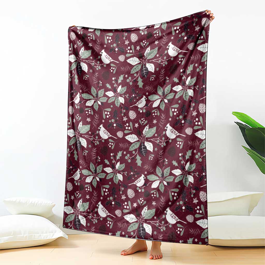 Wine red blanket with repeating white bird and poinsettia pattern, draped on floor.