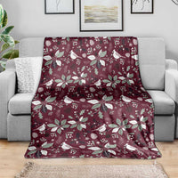 Wine red Christmas blanket with white birds and poinsettia flowers, spread over sofa.