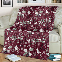 Wine red blanket with white poinsettias, leaves, and birds pattern, shown on couch.