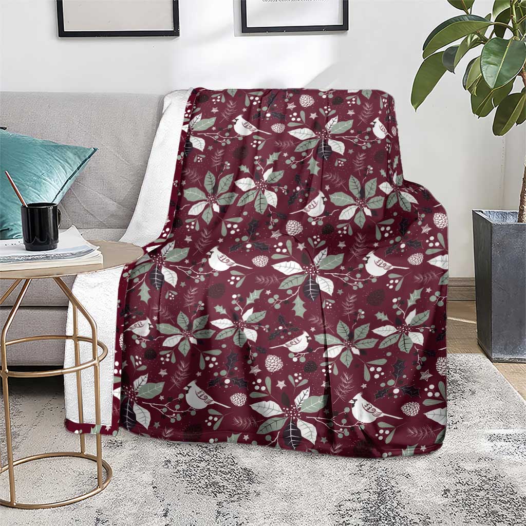 Wine red Christmas throw blanket with white bird and poinsettia motifs, draped on chair.