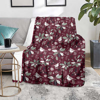 Wine red Christmas throw blanket with white bird and poinsettia motifs, draped on chair.