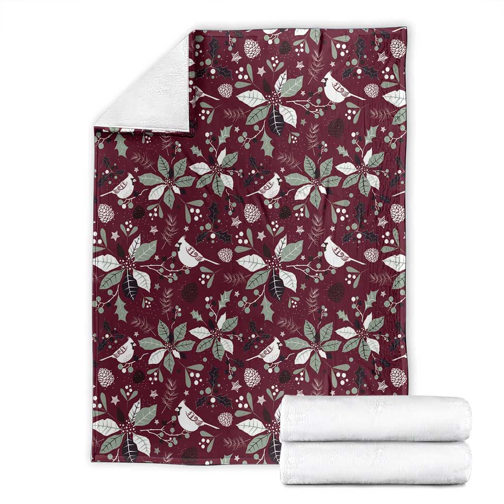 Wine red blanket with repeating white poinsettia and bird pattern; neatly folded.