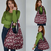 Wine red holiday tote bag with white botanical pattern shown being carried with dual handles