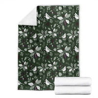 Green Christmas blanket with white bird and foliage pattern, shown with folded towels