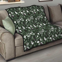 Green Christmas quilt with white bow-and-leaf pattern, draped over a gray couch