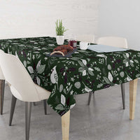 Green Christmas tablecloth with white bird, leaf, and pinecone motifs across table.