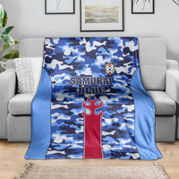 Blue camouflage blanket with Samurai Blue lettering and red torch emblem, laid on couch