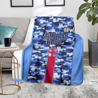 Blue camouflage blanket with Samurai Blue text and red torch crest, resting on gray rug