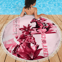 Pink round beach blanket with fringe edge, horse and lily graphic, spread on wooden deck.