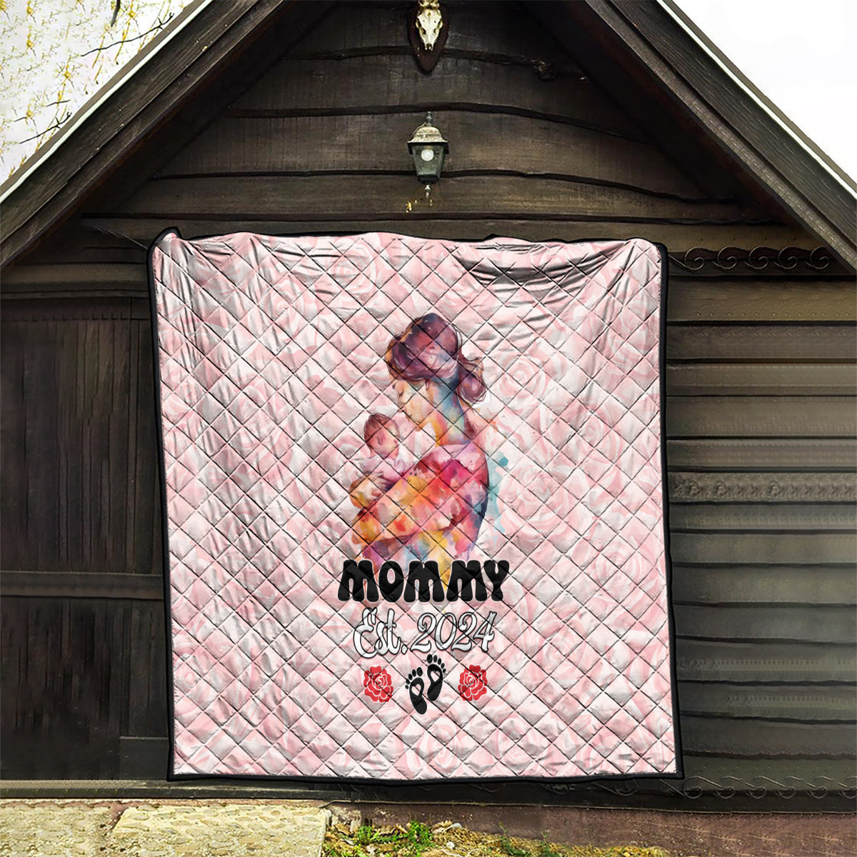 Pink quilt hung on a wooden porch, showing mom-and-baby graphic and 'Est. 2024'.
