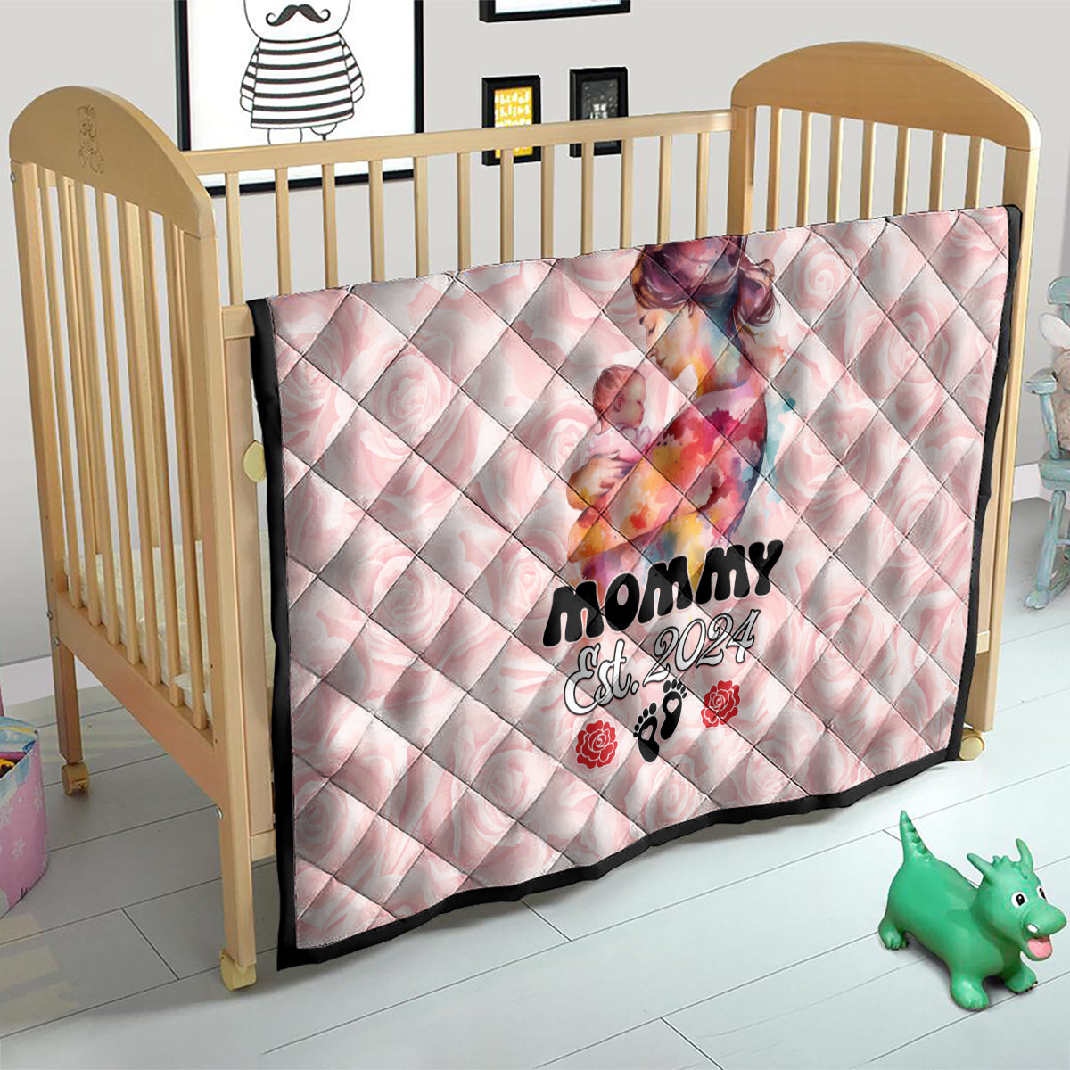 Pink quilt on a baby crib with mom-and-baby graphic and 'Mommy Est. 2024' wording.