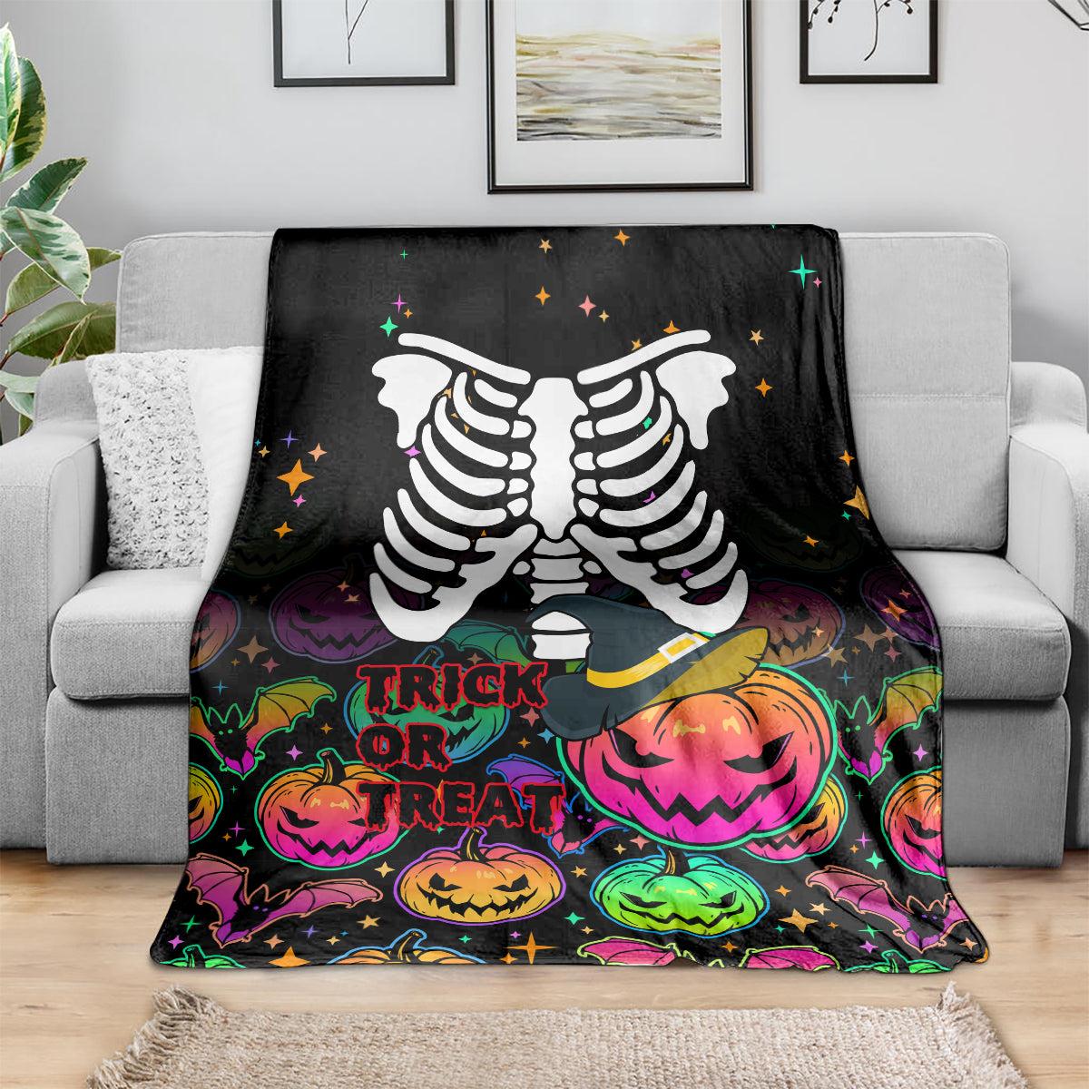 Black Halloween skeleton blanket draped over gray couch, trick-or-treat pumpkin graphics