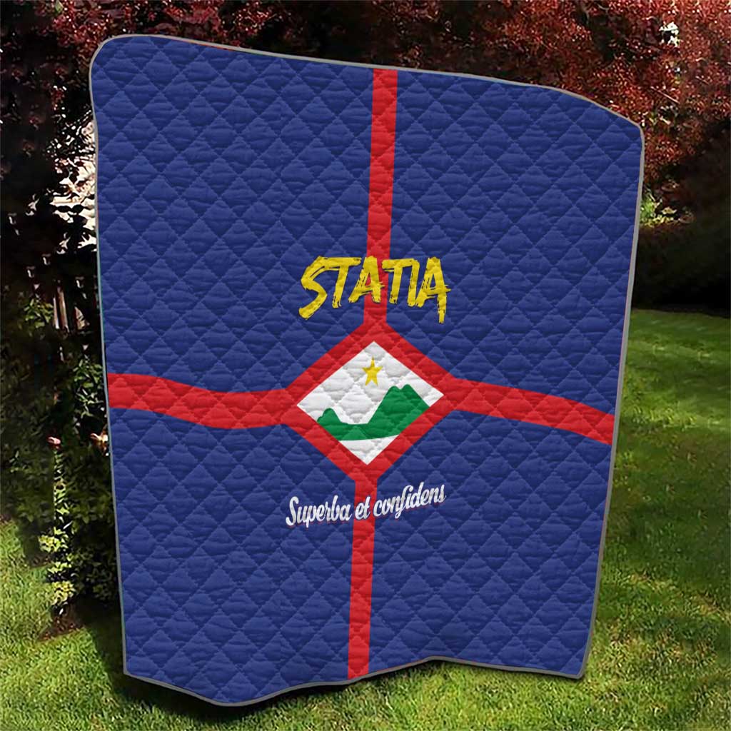 Blue quilt folded in yard with red cross and Statia crest, yellow STATA and Superba text