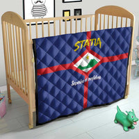 Blue quilt draped on toddler bed, red cross with Statia crest and yellow STATA logo