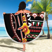 Black round beach blanket with colorful shield print, white fringe, and hibiscus flowers