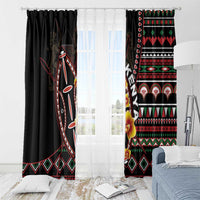 Black window curtain set with bold red, green, and white tribal shield panels over a bed