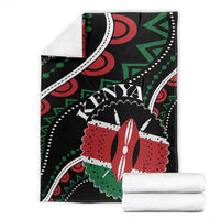 Black Kenya blanket with red, green, white designs, folded with matching white fabric roll