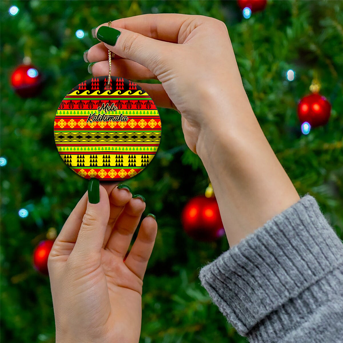Ceramic circle Christmas ornament with Hawaiian quilt pattern, red/yellow/green, held by hand