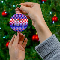Blue circular ceramic Christmas ornament held by hand, with Croatian embroidery pattern.