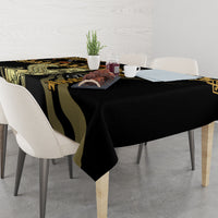 Black tablecloth with gold and green decorative print, covering dining table with plates