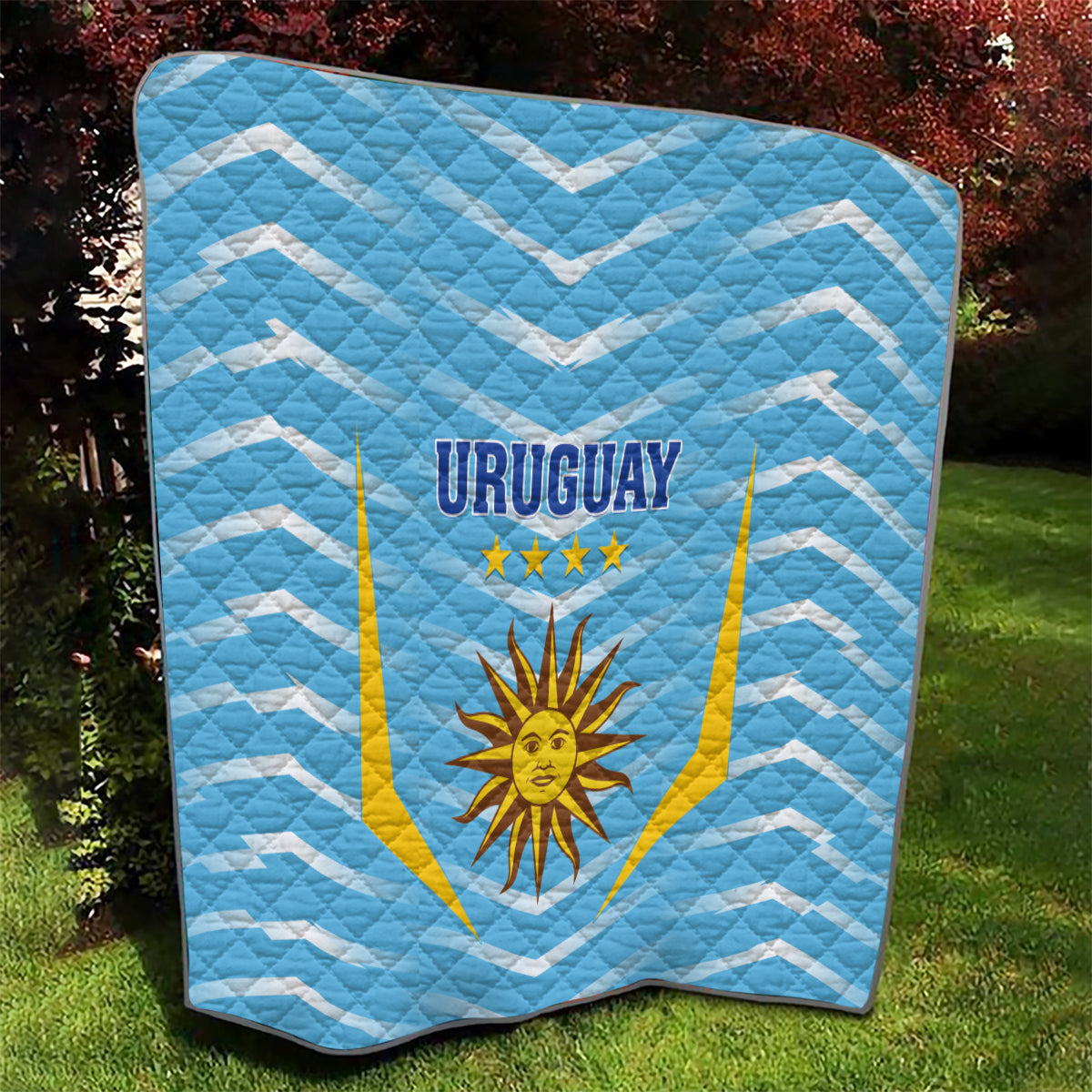 Light blue quilt showing 'URUGUAY' and sun emblem inside gold-lined shield, zigzag pattern