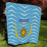 Light blue quilt showing 'URUGUAY' and sun emblem inside gold-lined shield, zigzag pattern