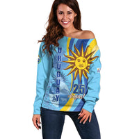 Women’s light blue off-shoulder sweater with large sun graphic and Uruguay flag stripes