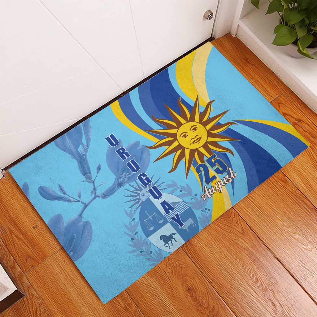 Blue rubber doormat with sun emblem and “25 August” graphic, angled on wooden floor
