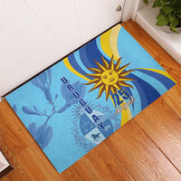 Blue rubber doormat with sun emblem and “25 August” graphic, angled on wooden floor