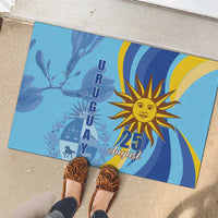 Blue rubber doormat with sun emblem and “25 August” text, shown with shoes