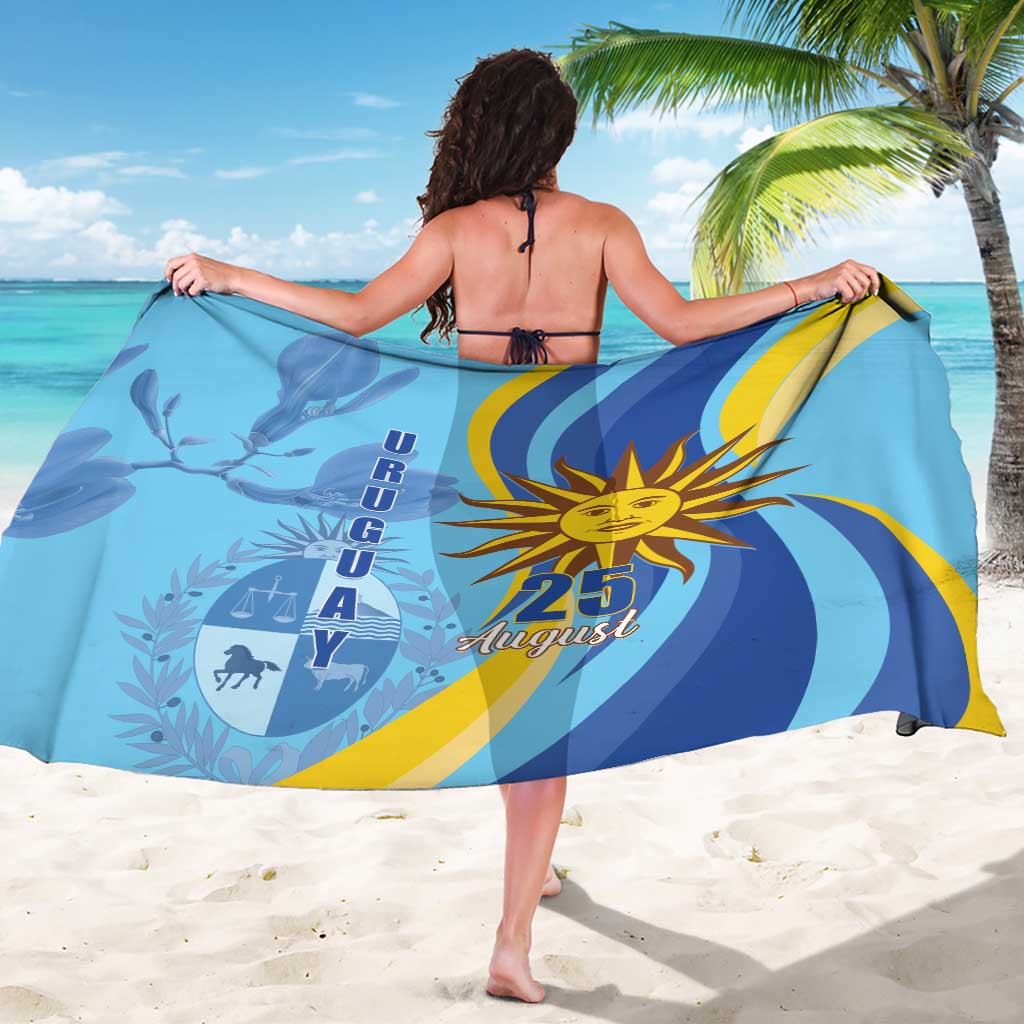 Blue sarong with sun emblem and 25 August text, held wide like a cape.