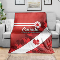 Red and white Canada flag blanket with maple leaf graphics, spread across a gray sofa