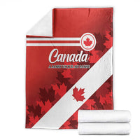 Red and white Canada flag blanket with maple leaf design, folded with stacked throws