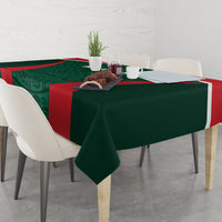 Green tablecloth with red stripe and patterned center, laid across table with dishes