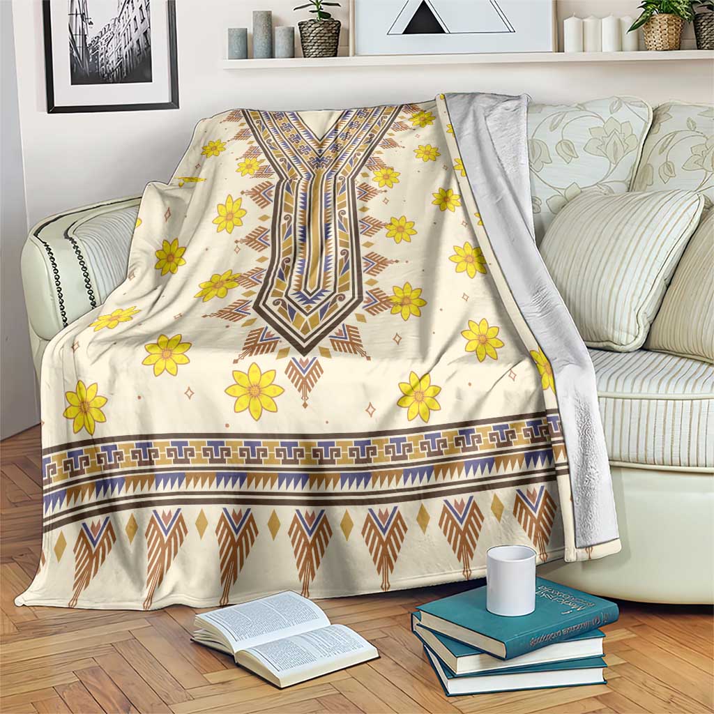 Cream blanket with yellow flowers and blue geometric dashiki pattern, draped on couch