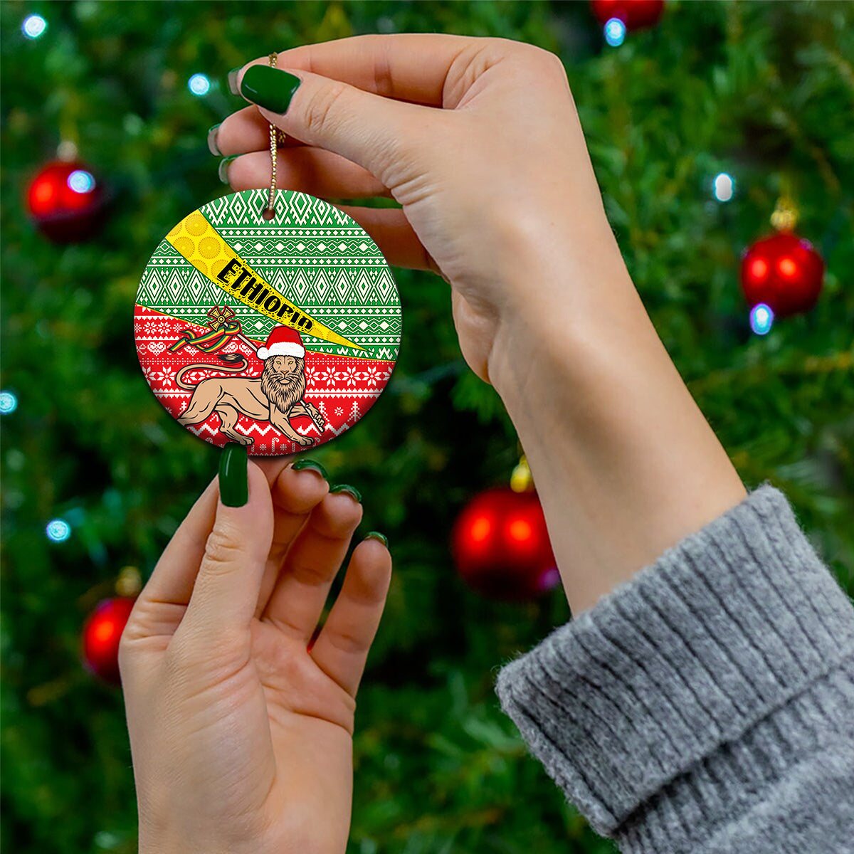 Hand holding round ceramic Christmas ornament with green red Ethiopian pattern and ETHIOPIA band.