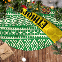 Christmas tree skirt close-up with green geometric bands, red motifs, and yellow accents