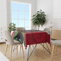 Red tablecloth with black, green, and yellow polynesian pattern over dining table