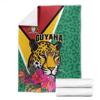 Stacked green Guyana jaguar blanket with pink flowers beside white towels