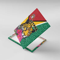 Diagonal view of green canvas wall art showing a jaguar portrait, pink flowers, and Guyana lettering
