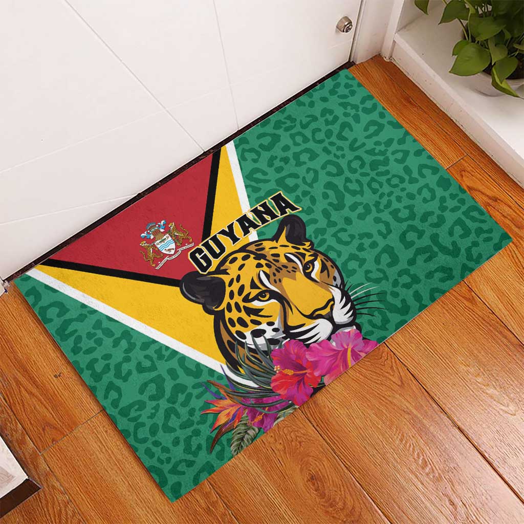 Green rubber doormat angled on wood floor, jaguar head with Guyana logo and flowers